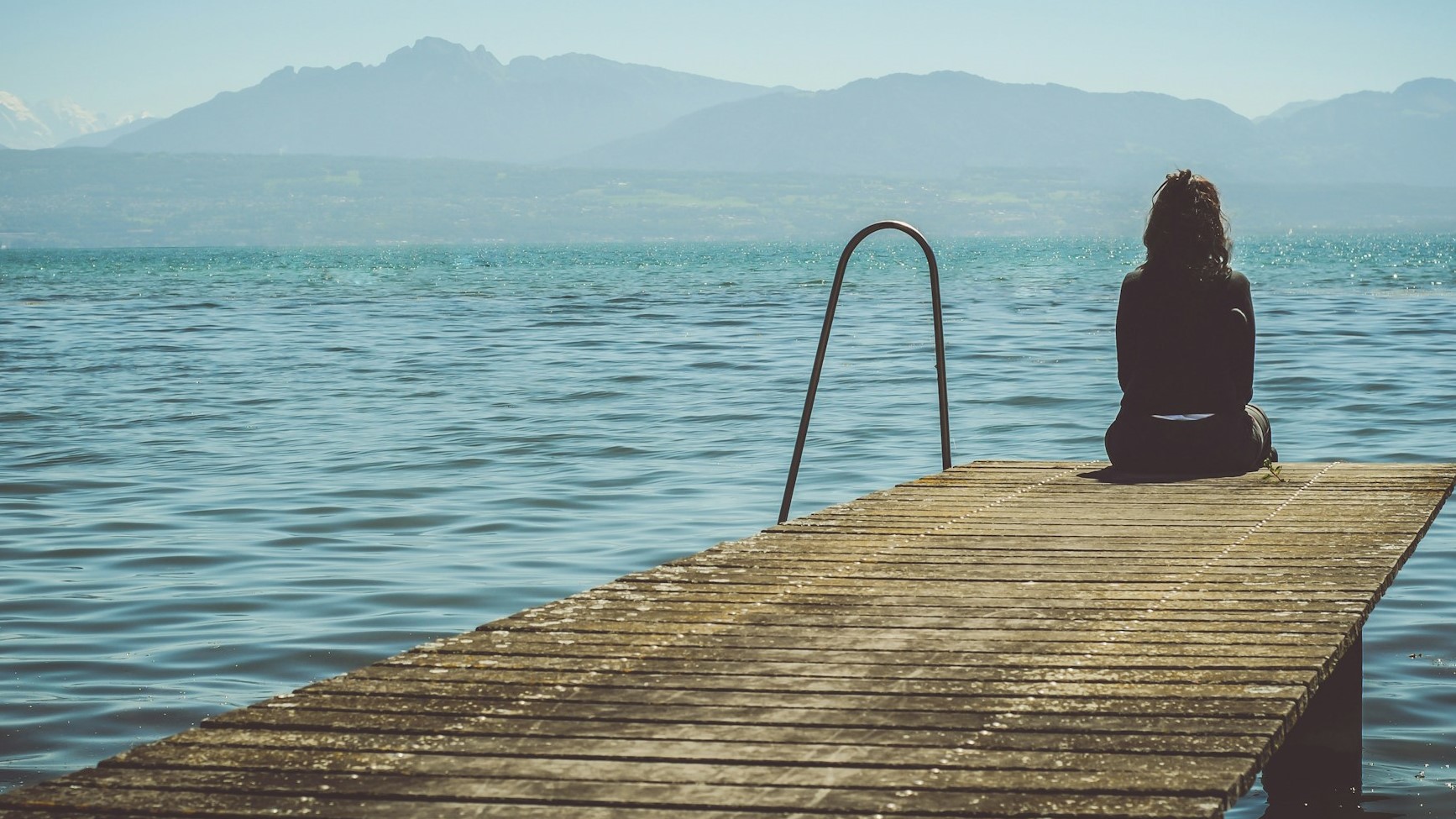 Kvinna som sitter ensam på en brygga vid vattnet